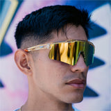 Front lifestyle view of LosReyes Prime Galaxy Sun wraparound yellow sports sunglasses with gold mirrored lens and amber speckled frame, modeled outdoors for versatile athletic use in sunlight.
