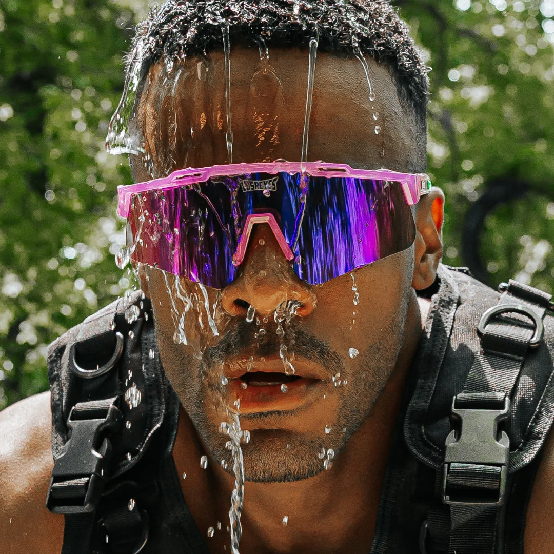 Lifestyle shot of LosReyes Prime Jurassic Brontosaurus sunglasses in pink and purple with a mirrored shield lens, captured mid-action with water splash during intense outdoor athletic performance. Wraparound fit designed for speed, durability, and UV protection.