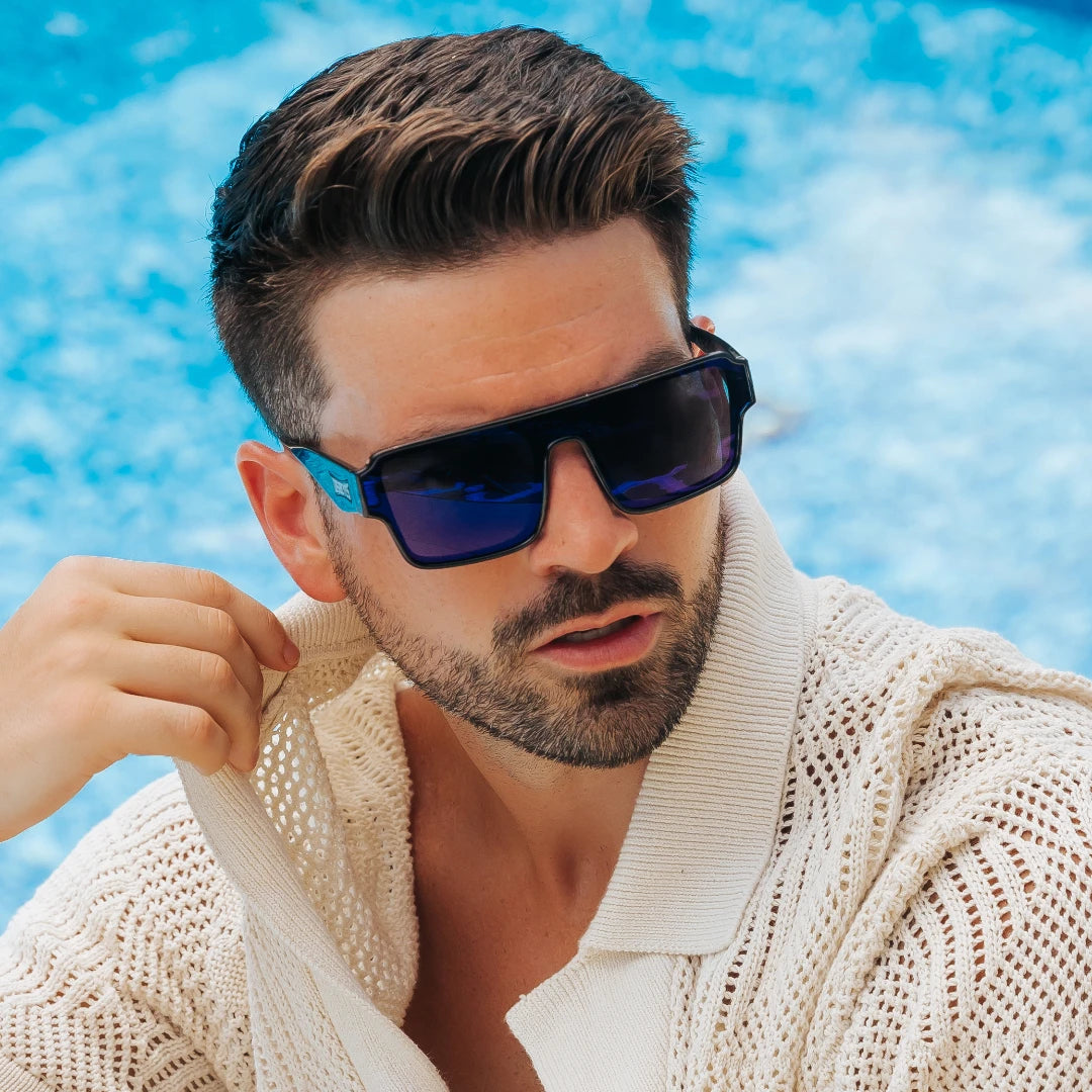 Man wearing LosReyes Poseidon blue sunglasses and a beige sweater by a pool