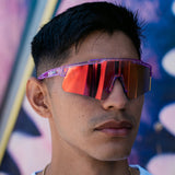 Lifestyle photo of a man wearing LosReyes Prime Galaxy Mercury mirrored sports sunglasses with translucent purple frame and orange shield lens—combining streetwear flair with athletic utility.