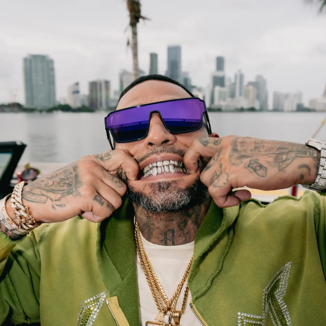Man wearing LosReyes Zeus sunglasses and a green jacket with a city skyline in the background