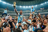 Lionel Messi lifting the FIFA World Cup trophy in celebration, surrounded by cheering fans and teammates inside a packed stadium