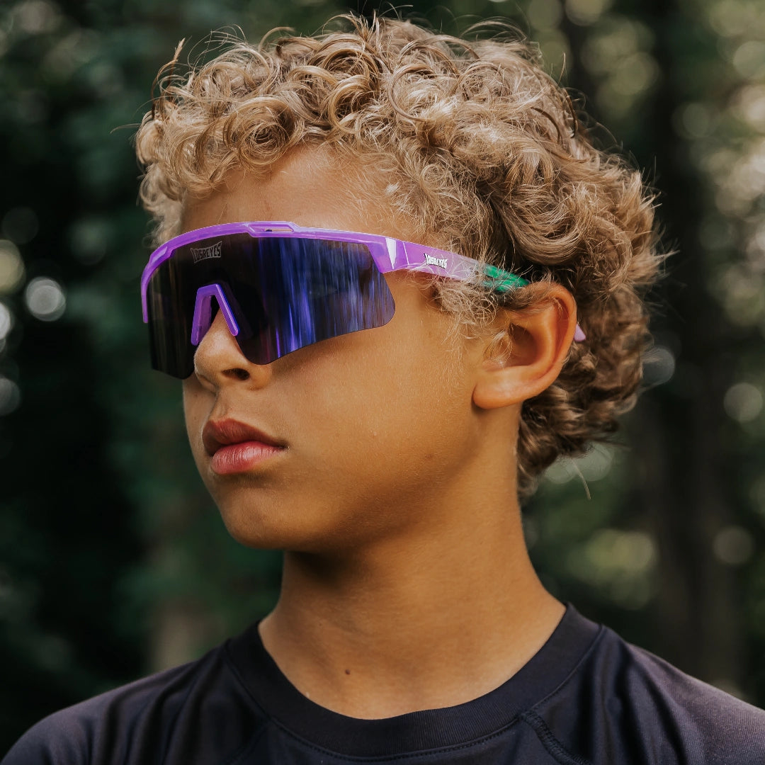 Youth lifestyle photo of LosReyes Prime Jurassic Brontosaurus sunglasses in purple and green with a mirrored shield lens, designed for young athletes with a wraparound fit and outdoor performance protection.