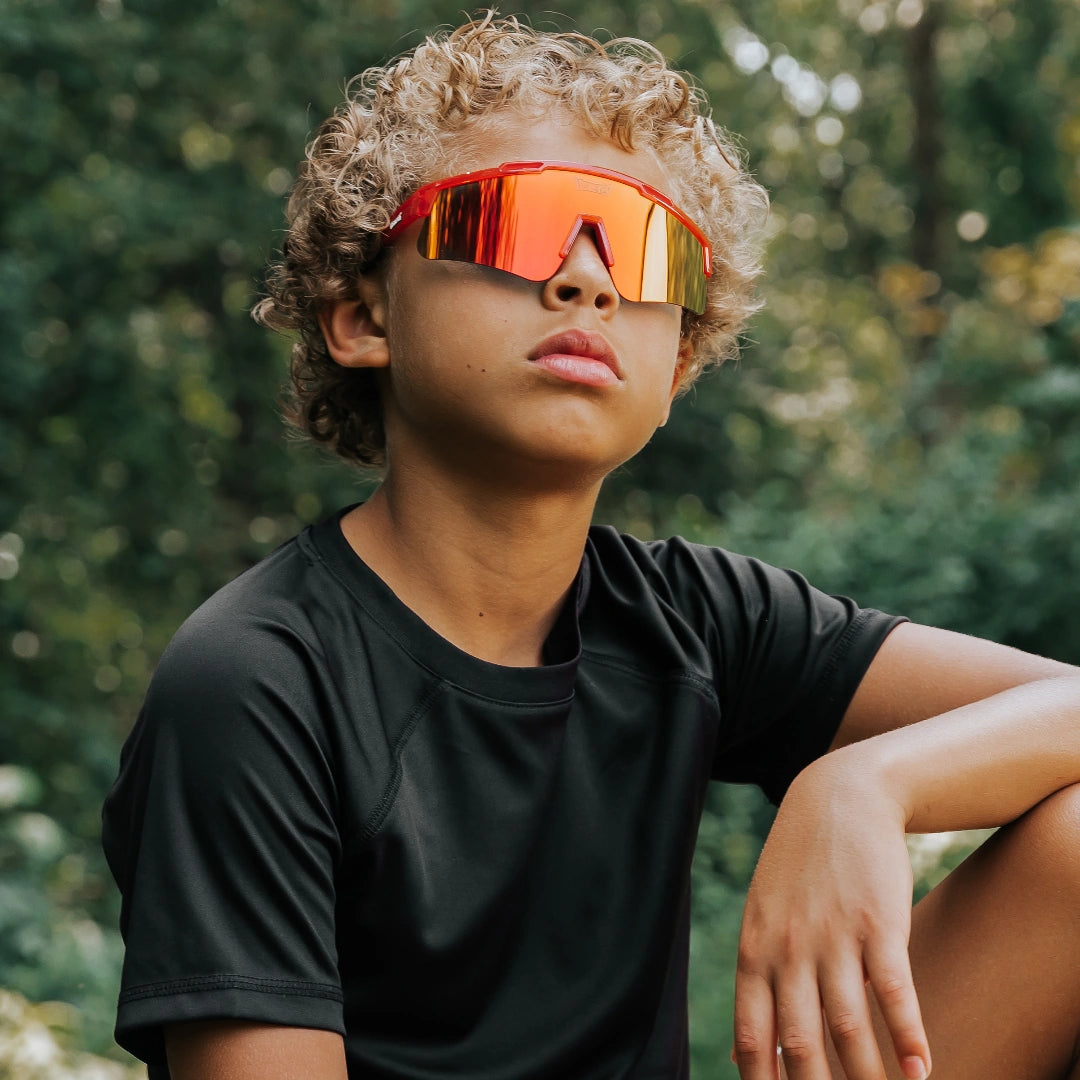 Youth lifestyle photo of LosReyes Prime Jurassic T-Rex red sports sunglasses with mirrored shield lens and wraparound fit, engineered for active kids, UV protection, and outdoor adventure performance.

