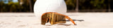 LosReyes Jupiter sunglasses from the Galaxy Collection resting in beach sand beside a volleyball.
