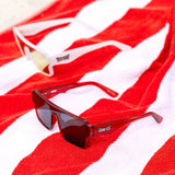 LosReyes red and white lifestyle sunglasses displayed on a striped beach towel, highlighting UV400 protection and high-fashion summer style.
