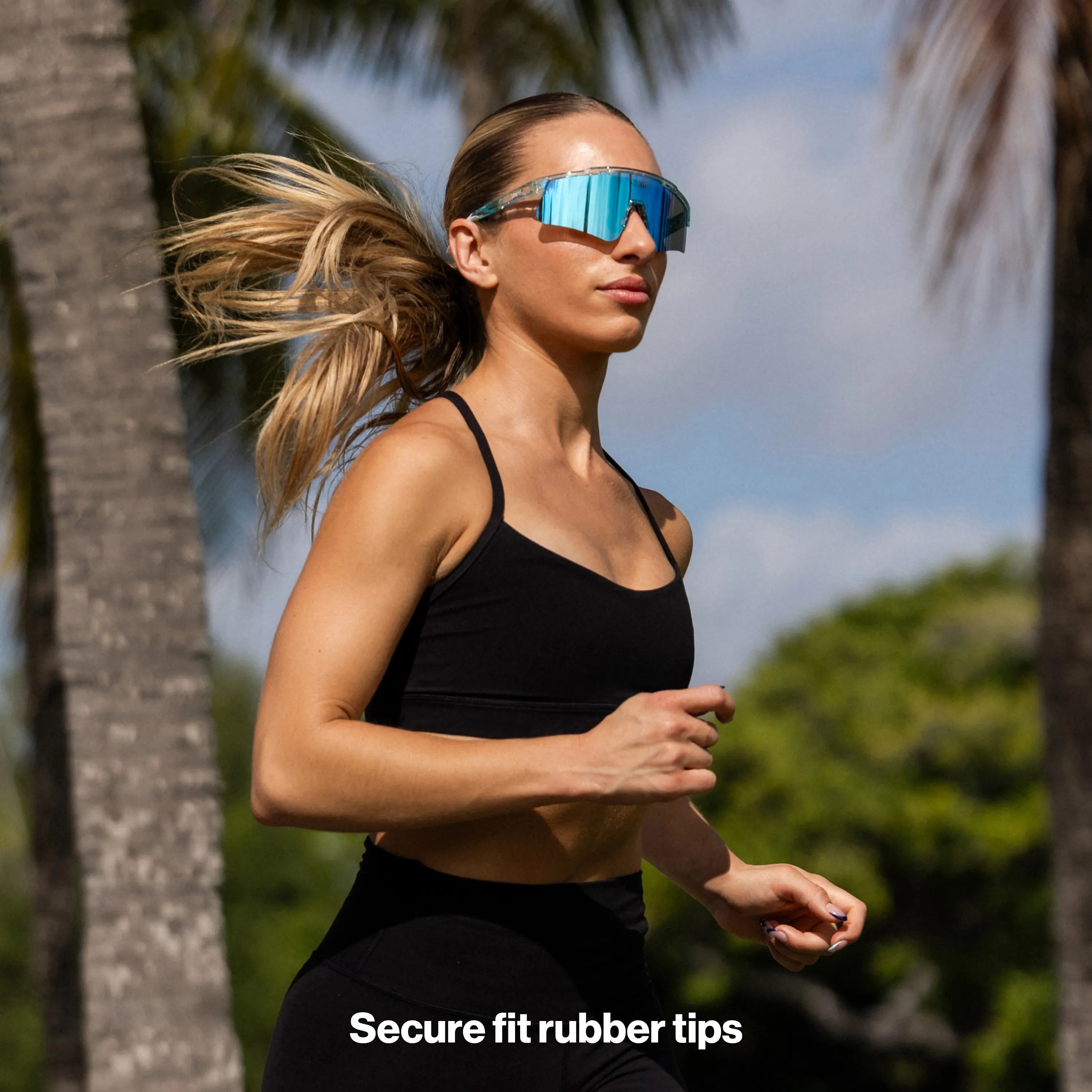 Female runner wearing LosReyes Uranus performance sunglasses while jogging in a palm-tree outdoor setting.
