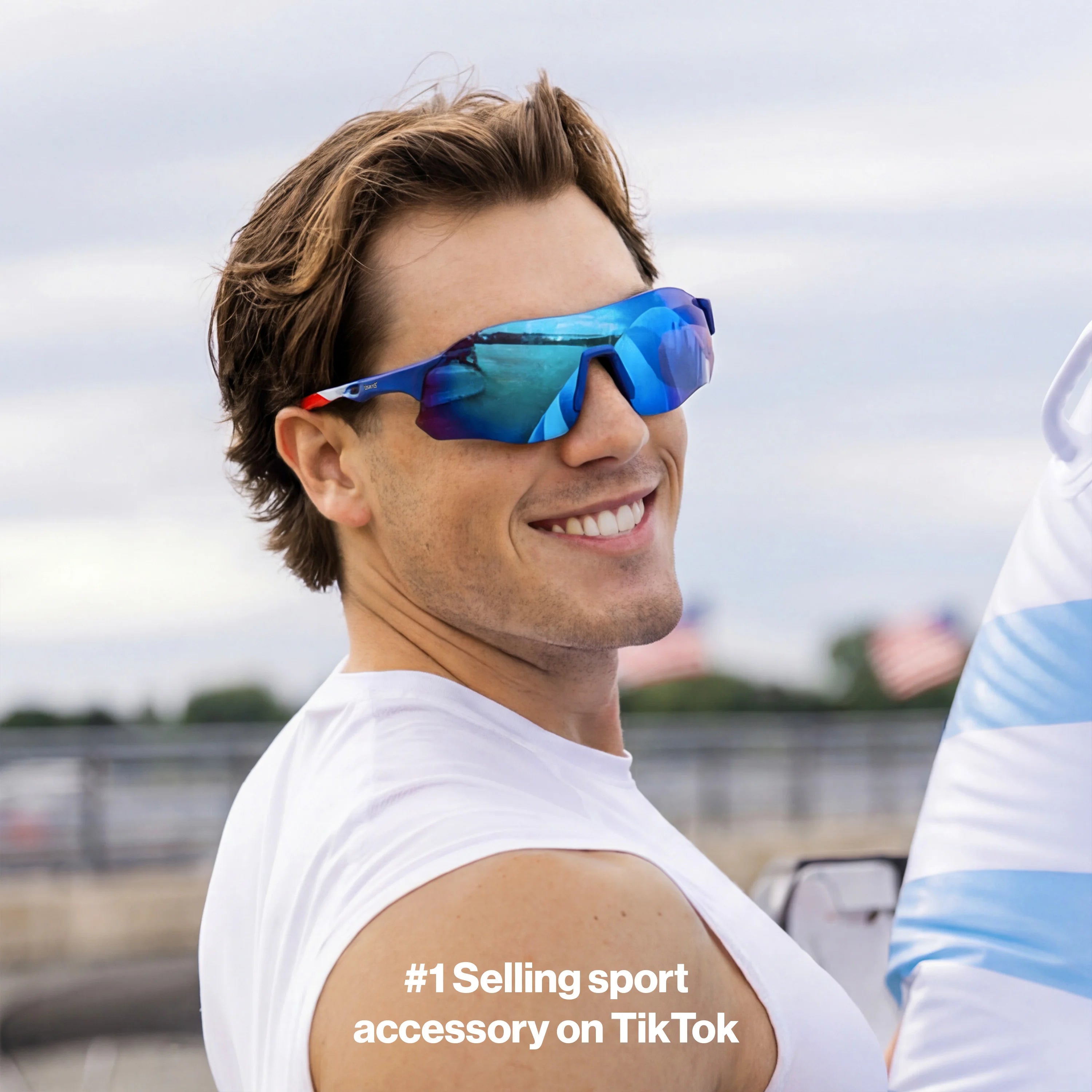 Man in white tank top smiling outdoors wearing LOSREYES Edge USA 250 limited edition running sunglasses with red white and blue frame and blue mirrored lens
