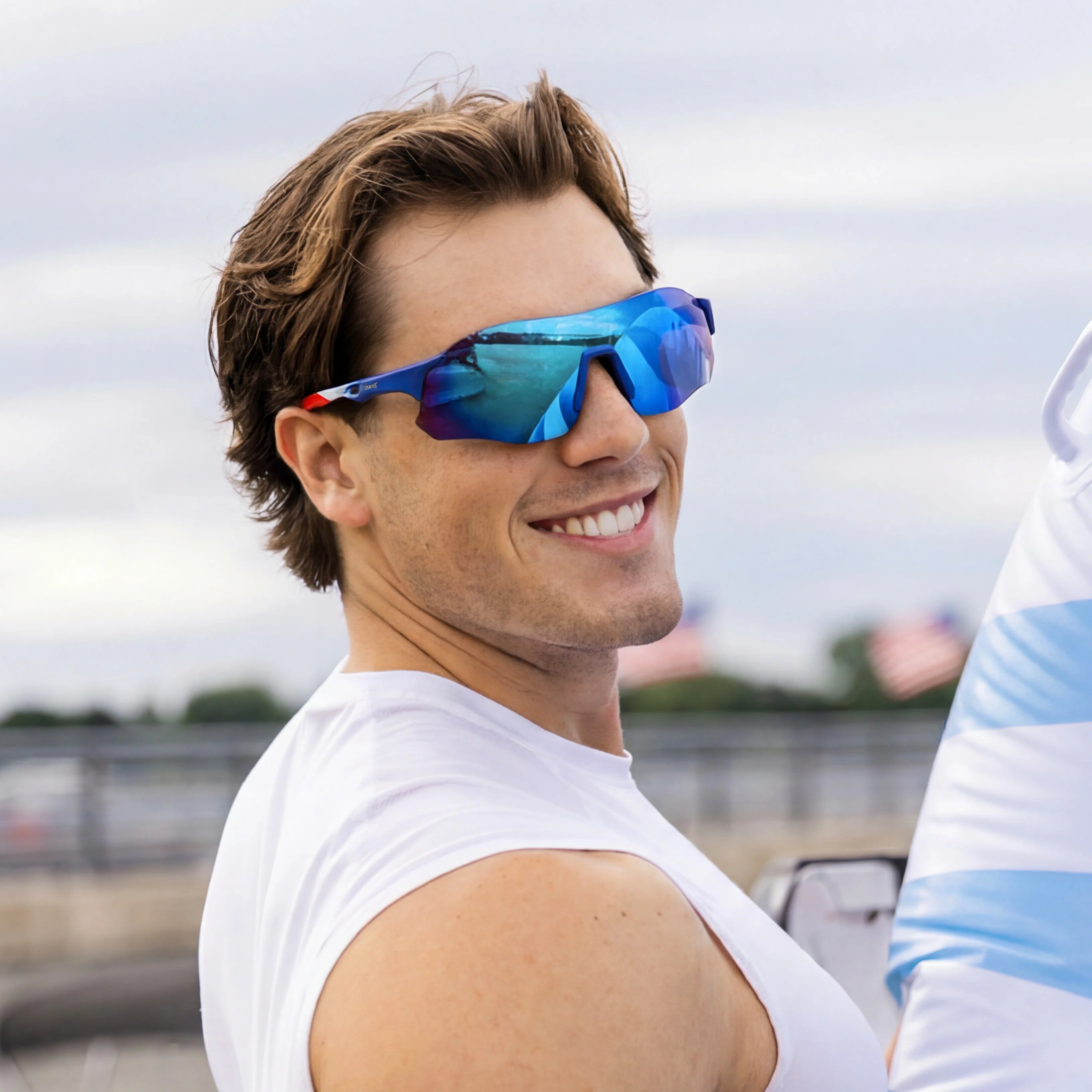 Man in white tank top smiling outdoors wearing LOSREYES Edge USA 250 limited edition running sunglasses with red white and blue frame and blue mirrored lens