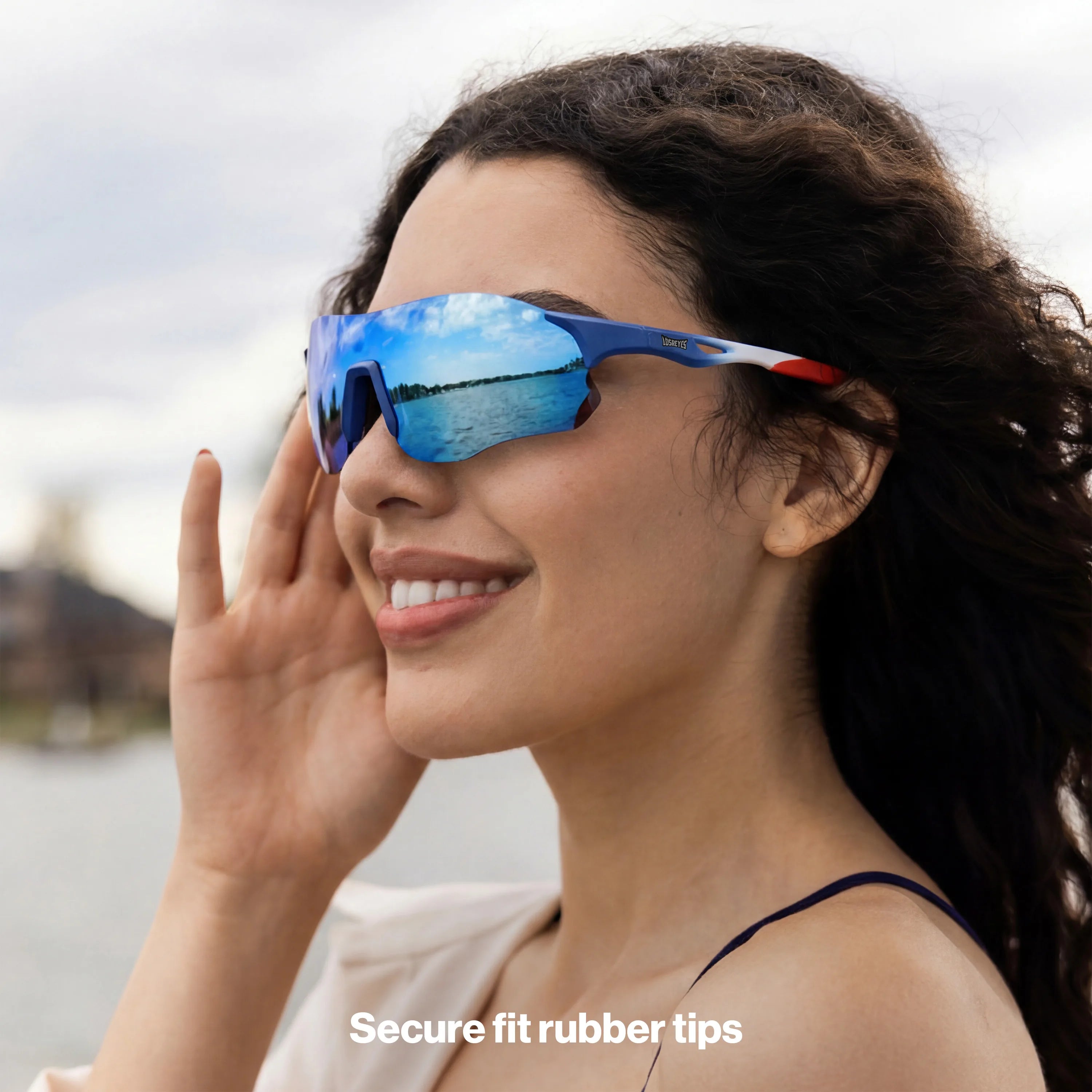 Woman with curly dark hair smiling by the water wearing LOSREYES Edge USA 250 limited edition running sunglasses with red white and blue frame and blue mirrored lens
