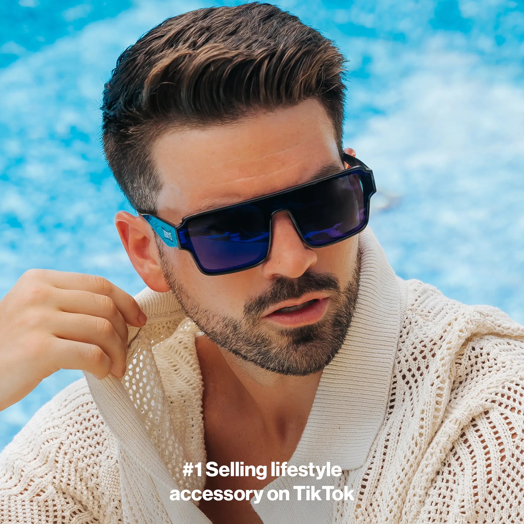Man wearing LosReyes Poseidon blue sunglasses and a beige sweater by a pool
