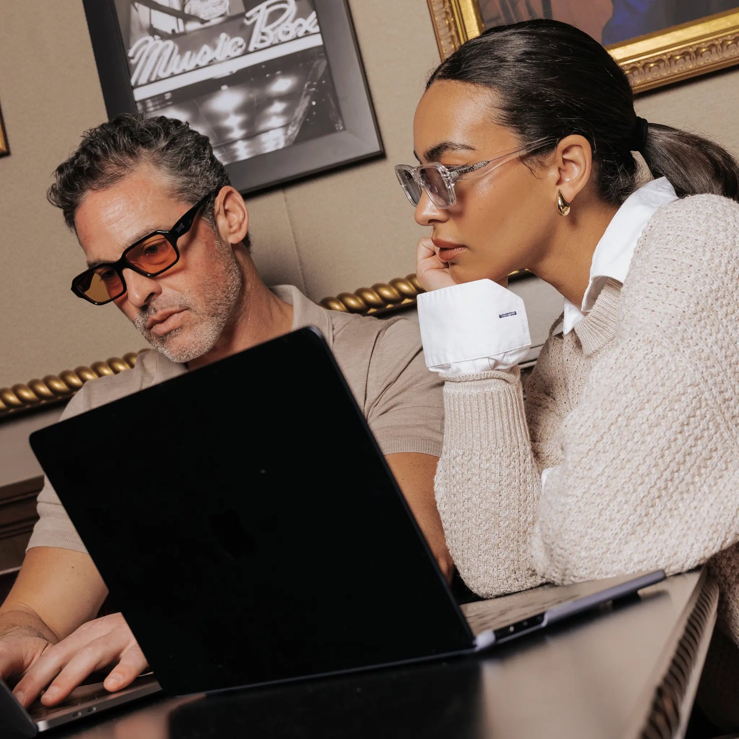 Luxury LosReyes Opus sunglasses worn by stylish couple working on laptop in cafe – transparent Monaco frames and black Positano frames with orange lenses