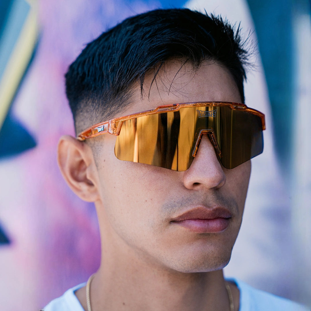 Lifestyle front view of LosReyes Prime Galaxy Jupiter performance sunglasses in orange with gold mirrored lenses, styled for streetwear-meets-sport appeal.