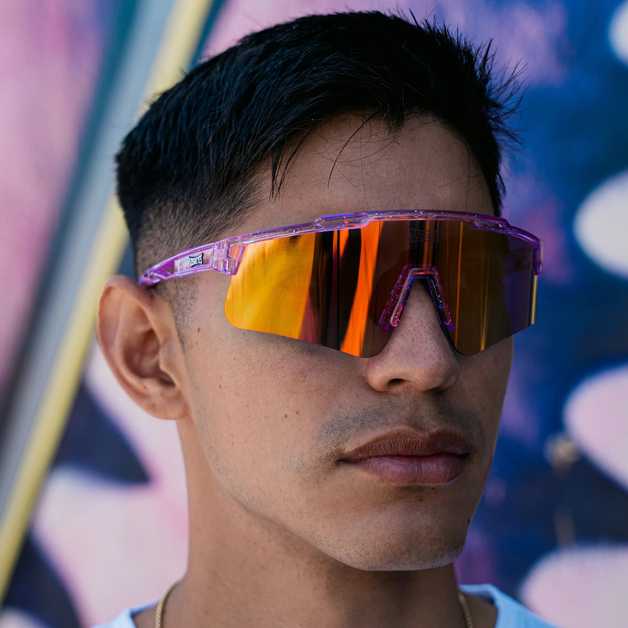 Lifestyle photo of a man wearing LosReyes Prime Galaxy Mercury mirrored sports sunglasses with translucent purple frame and orange shield lens—combining streetwear flair with athletic utility.