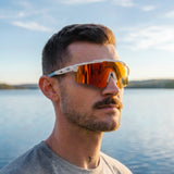 Man wearing LOSREYES Prime USA 250 Limited Edition sunglasses with white speckle frame and red mirror lens by a summer lake at sunset