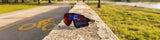 LosReyes SHOWTIME sunglasses resting on stone wall beside bike path, featuring mirrored performance lens for cycling